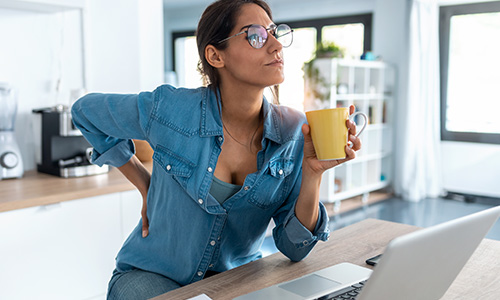 Woman sitting at home touching her lower back