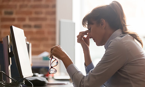 A woman touching her nose looking at her work computer tensely