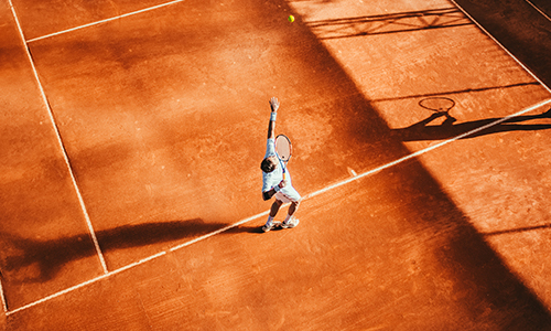 Man serving a tennis ball on a clay court