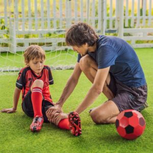 Adult checking child's leg injury on soccer field