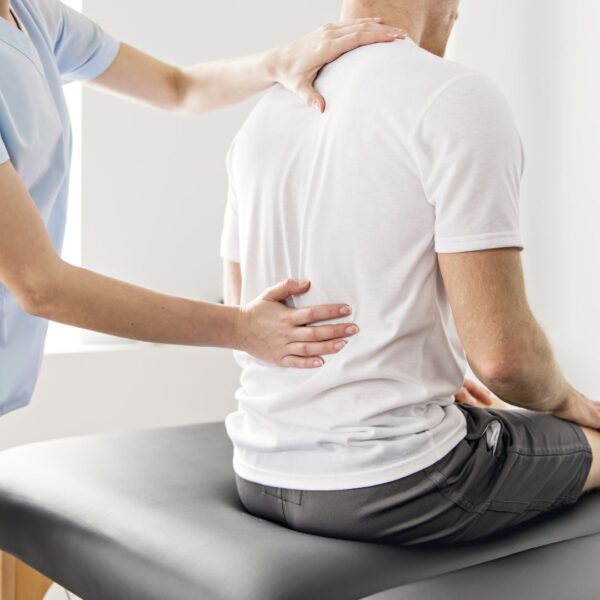 A chiropractor in a light blue tunic places her hands on a male patient's back during a spinal alignment.