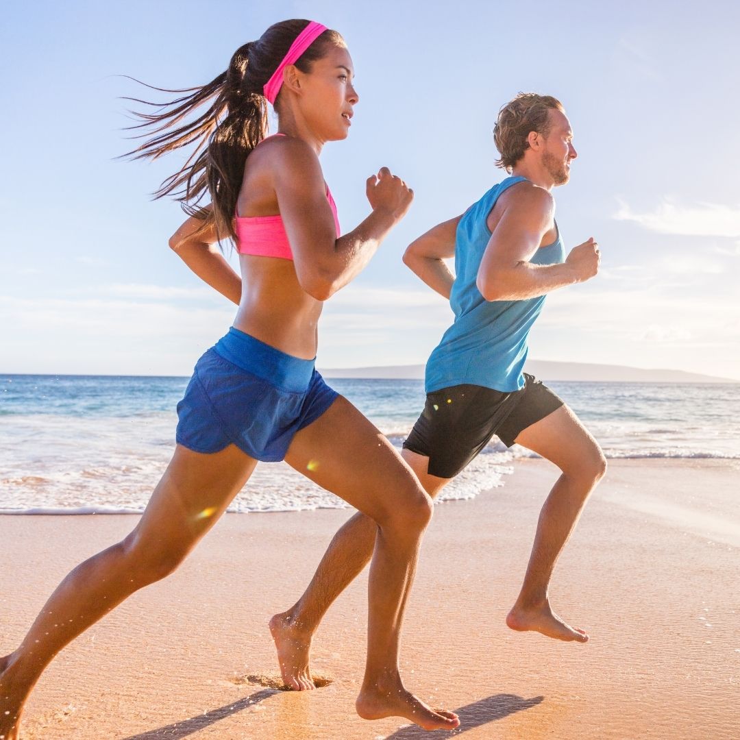 A man and woman run barefoot on a sandy beach, representing the physical activity pillar of wellness.