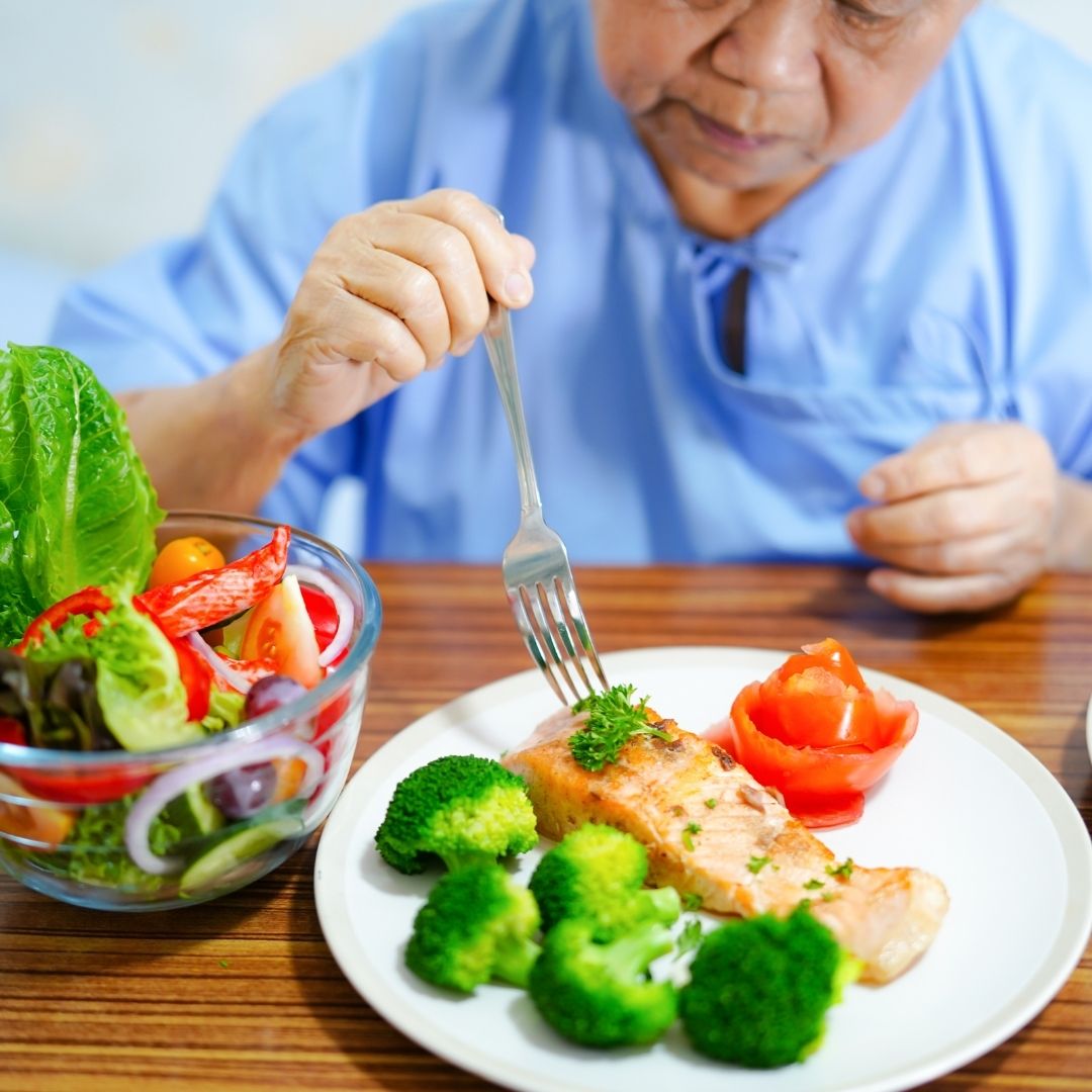 An older patient eats a healthy meal of salmon, broccoli, and salad, representing the nutrition pillar of wellness.