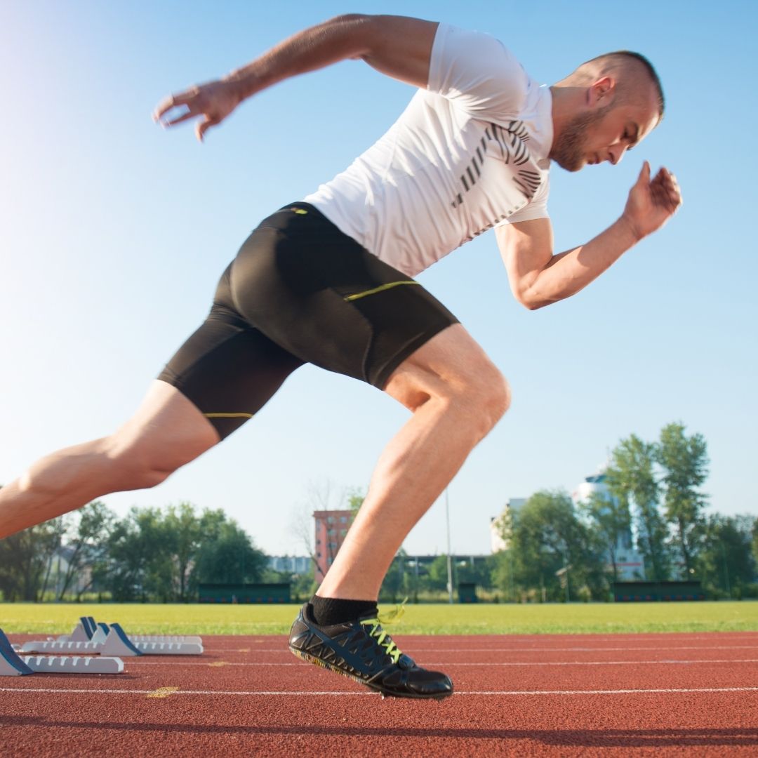 A male athlete explodes from the starting blocks, sprinting on a running track.